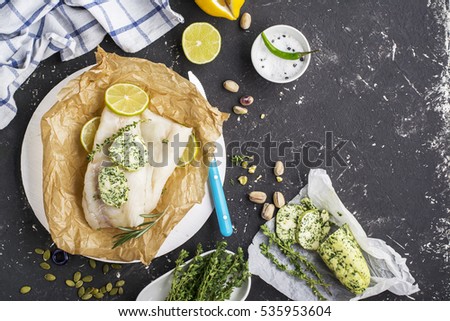 Fresh cod before baking with homemade green butter with herbs on a dark background with slices of lemon, thyme, sea salt. Top view. Healthy food concept