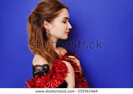 Portrait of a girl in evening black velvet dress and red shiny tinsel. New Year is coming soon. Girl thinks it's time to give gifts for a holiday. Big Christmas season sales and discounts. 