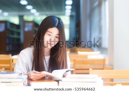 Happy asian student  young woman thinking with book in library sitting on wood table
