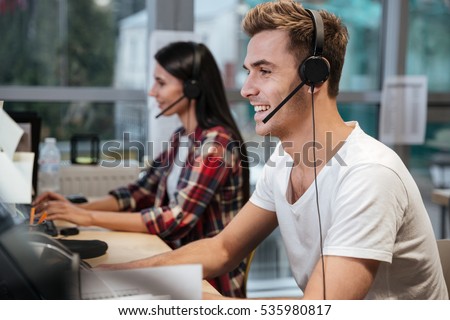 Side view of Smiling Coworkers sit by the table in headphones. Call center Royalty-Free Stock Photo #535980817