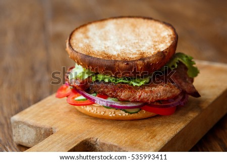 Classic american fast food background. Burger with roasted open roasted bun and grilled on barbecue meat with onions on wooden cutting board. Hamburger with fresh vegetables composition.