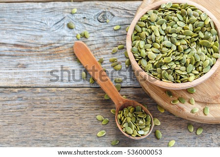 Bowl with pumpkin seeds and a wooden spoon on a wooden table.