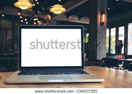 Mockup image of laptop with blank white screen on wooden table in dark modern cafe Royalty-Free Stock Photo #536021305