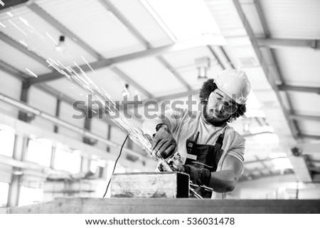 Young manual worker using grinder on metal in factory
