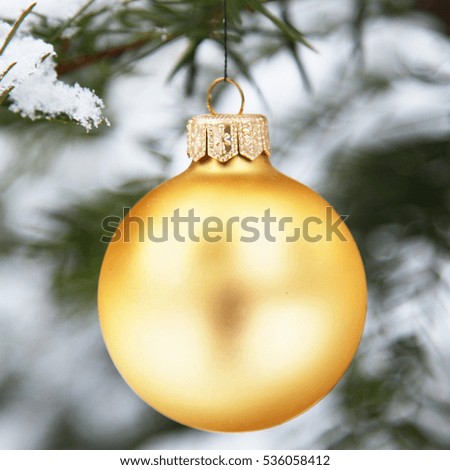 Gold Christmas tree ball on Christmas fir branch in snow outdoors