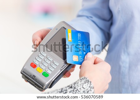 Hand holding contactless credit or debit card over wireless payment terminal at shop Royalty-Free Stock Photo #536070589