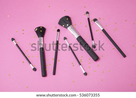 Cosmetic make up brushes on a hot pink background with gold sparkly stars