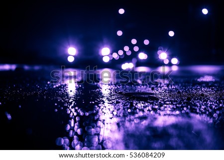 Rainy night in the big city, the cars traveling towards the headlights illuminate the road. Close up view from the level of the dividing line, image in the purple-blue toning
