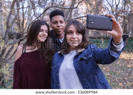 Group of young people, two caucasian girls and a black boy doing a selfie in the field with a cell phone. They are friends. 