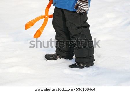 Children's winter games outdoors. The image of the child who is using a plastic toy makes balls-snowballs from snow.