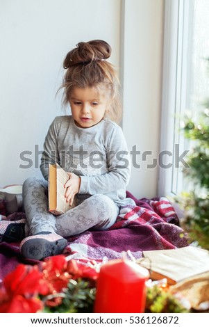 A child reads a book on the windowsill. The concept of Christmas