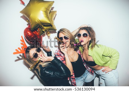 Three female friends posing in front of white wall. New year party