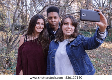 Young people of different races taking a selfie with the smartphone in the park. They are friends and enjoy a nice day outdoors. 
