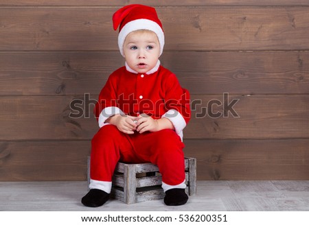 Boy dressed as Santa sitting on a wooden background