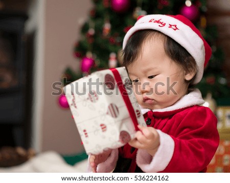 Asian baby girl in a Santa costume opening a gift box