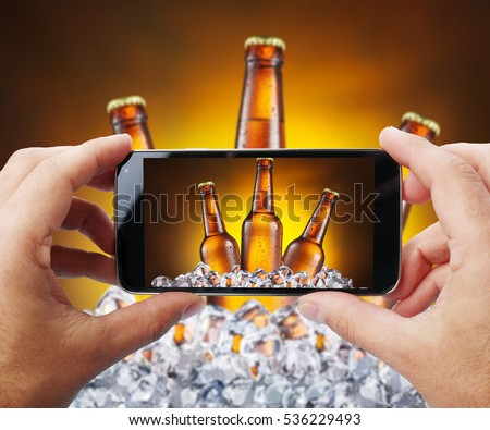 Taking photo of beer bottles in ice by smartphone. Closeup view of  process. File contains clipping paths for smartphone and hands and  picture on it.