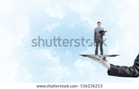 Hand of waiter presenting on tray man reading book