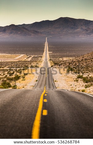 Classic vertical view of an endless straight road running through the barren scenery of famous Death Valley with extreme heat haze on a beautiful sunny day with blue sky in summer, California, USA Royalty-Free Stock Photo #536268784