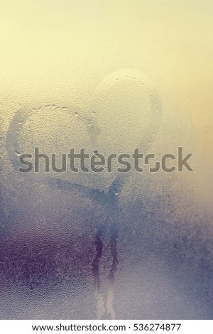 Abstract blurred love heart symbol drawn by hand on the wet frozen window door glass with sunlight background. Closeup of emotional image