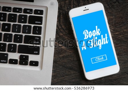 "Book A flight" words on smartphone with a laptop near it - website, multimedia and business concept