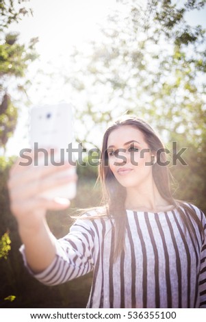Pretty brunette female model walking in the street with stunning natural light talking on her mobile phone and taking selfies
