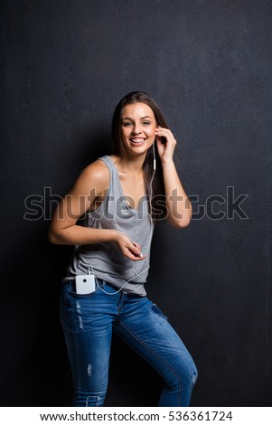 Beautiful brunette female model texting, taking a selfie, listing to music on her smart phone in a dark studio with edgy lighting