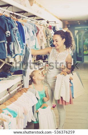 young mother with daughter buying baby pajamas in white color in kids section