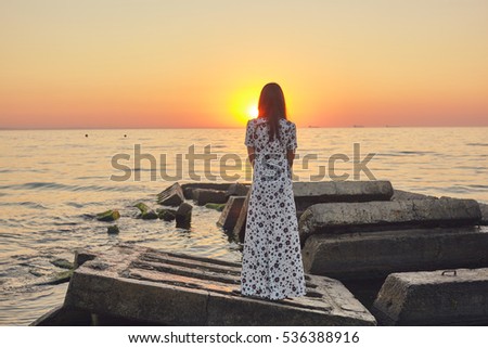 Beautiful girl in a white dress greets the dawn at sea