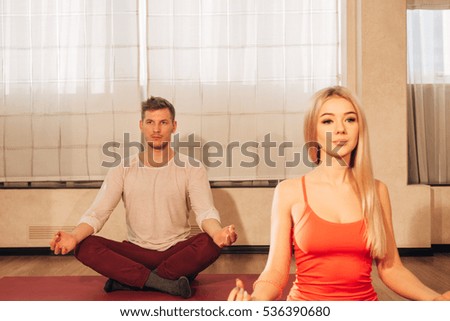 slim female and man on background meditating in pose of lotus in gym