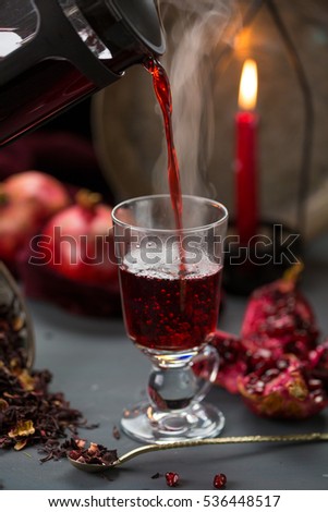 Pomegranate skin hot tea poured from jar with pomegranates and red candle in the background