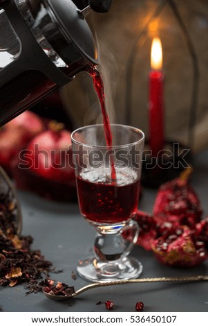 Pomegranate skin tea served hot and poured from jar with pomegranates and red candle in the background