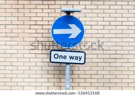 Blue Circular Sign White Direction Arrow One Way Fixed To One Pole In Front Of Brick Wall