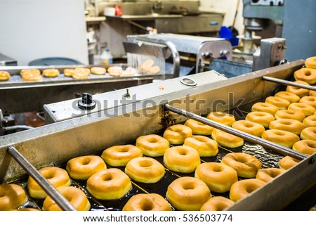 Donuts are fried, glazed, and put on racks in a doughnut shop bakery.  Royalty-Free Stock Photo #536503774