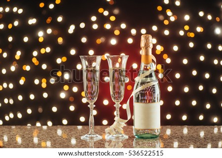 Christmas and New Year celebration with champagne. Pair of flute and bottle of Champagne for festive occasions against a dark background with gold shimmering light and bokeh