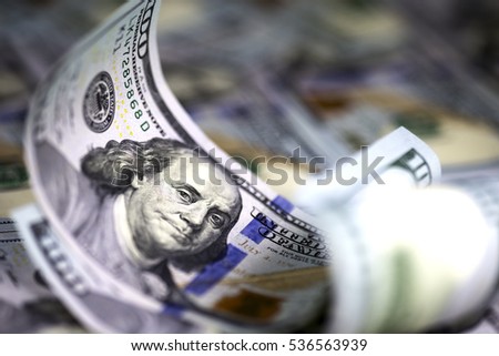 Several modern hundred us dollar bills, curved upward, lying on the background of hundred us dollar banknotes. Close up image. Selective light. Selective focus. 
