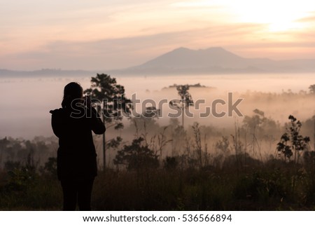 silhouette asian women photography take a photo with beautiful sunrise in environment fog in forest at Thung Salaeng Luang National Park Phetchabun Province,Thailand