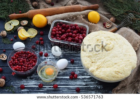 Cake pattern during prigotovleniya.Testo, flour, cherries, cranberries, lemons, eggs, nuts, and kitchen items on the black wooden table