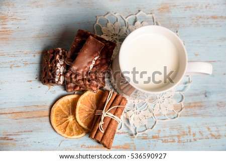 Christmas Chocolates with cup of milk, orange slices and cinnamon. Holiday Sweets in top view on blue painted background 
