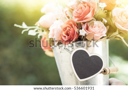 hands holding a pot flower in green meadow, with focus on heart tag, vintage picture style.