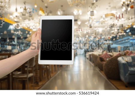 human hand hold smartphone, tablet, cell phone with blurry home decor store. concept of shopping and finding decoration for house decor interiors.