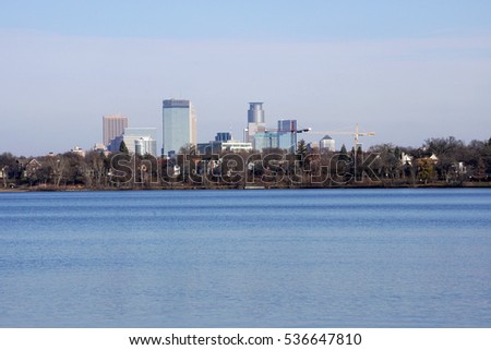 Minneapolis Minnesota skyline. Wide establishing photo skyscrapers tower over tree line and beautiful blue lake in winter. Buildings downtown financial district bank headquarters.