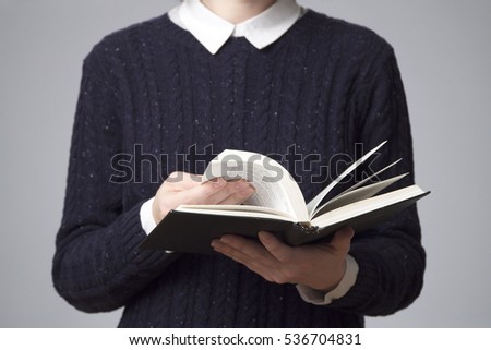 A woman in a blue sweater with a white collar reading a book, gray background
