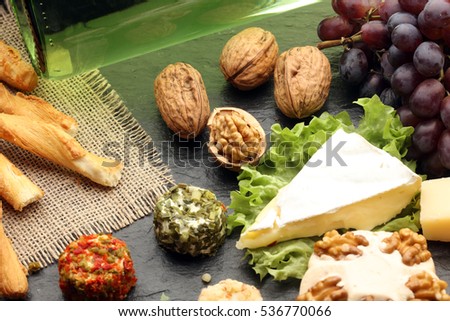 Assorted cheeses on round wooden board plate Camembert cheese, cheese grated bark of oak, hard cheese slices, walnuts, grapes, crackers, bread, thyme, dark black wood background
