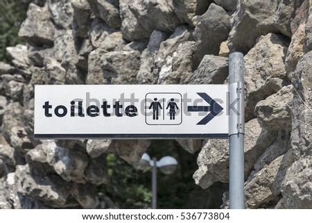 Toilet direction sign on white plate closeup outdoor
