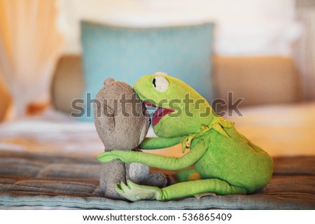 lovely soft green frog and brown bear lying on the bed