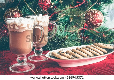 Christmas still life - two cups of winter hot drink cacao with marshmallows and chocolate cookies. Spicy hot chocolate on background of Christmas tree. Happy New Year. Moody style. Selective focus.