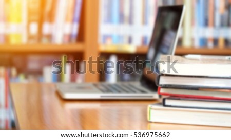 Book stack and laptop computer on workplace in library room with blurred bookshelf background, education concept 