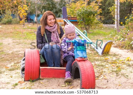 Little girl with her mother sitting at the children's home-made motorcycle in the yard