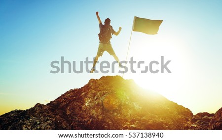 success, leadership, achievement and people concept - silhouette of young guy with flag on mountain top over sky and sun light background Royalty-Free Stock Photo #537138940