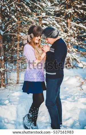 Happy couple: beautiful girl and handsome men enjoying each other in winter snowy forest. Men warming up girl's hands
